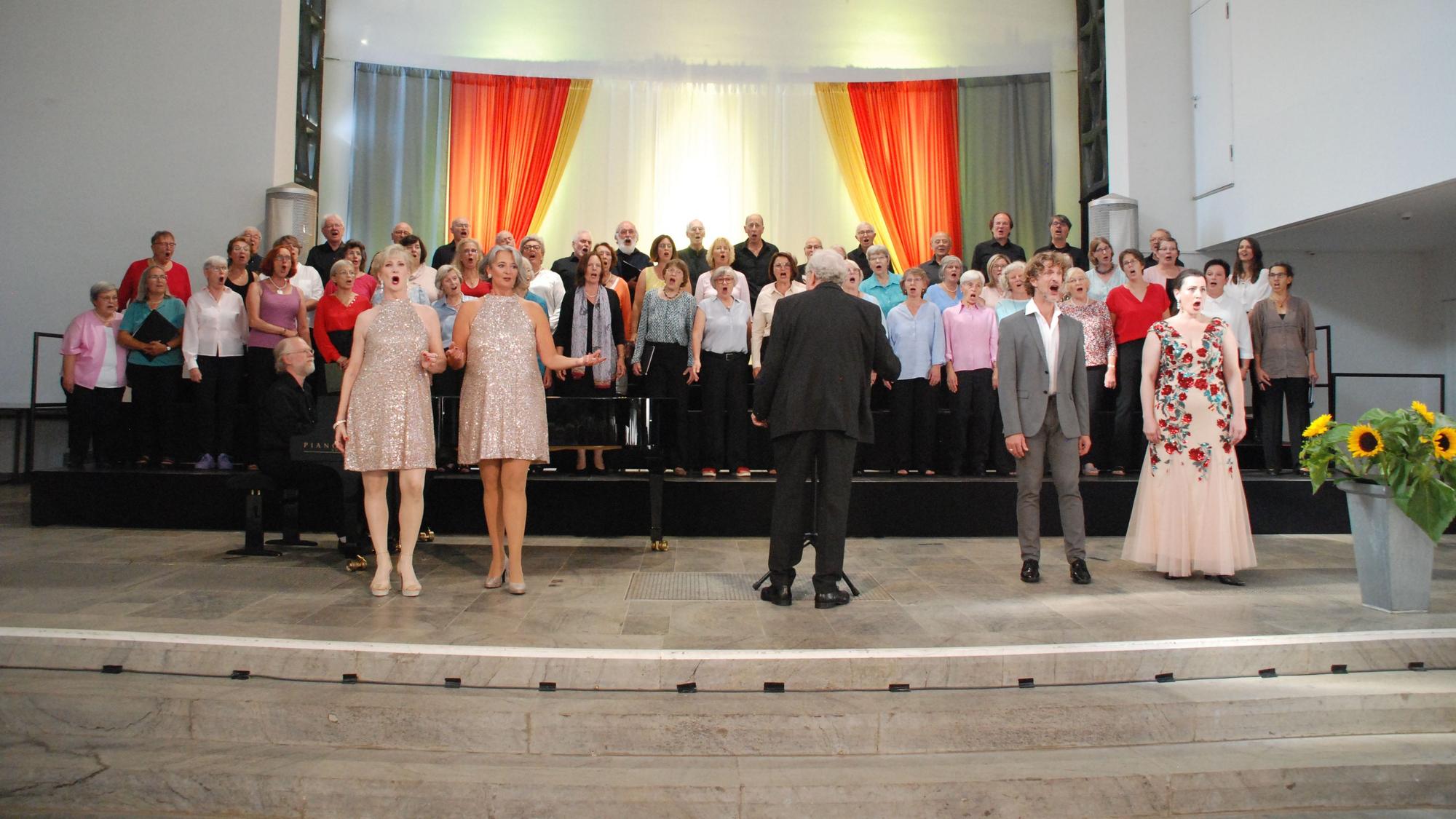 Auf einer Bühne singen ein Chor und Solisten, die vor der Gruppe stehen.