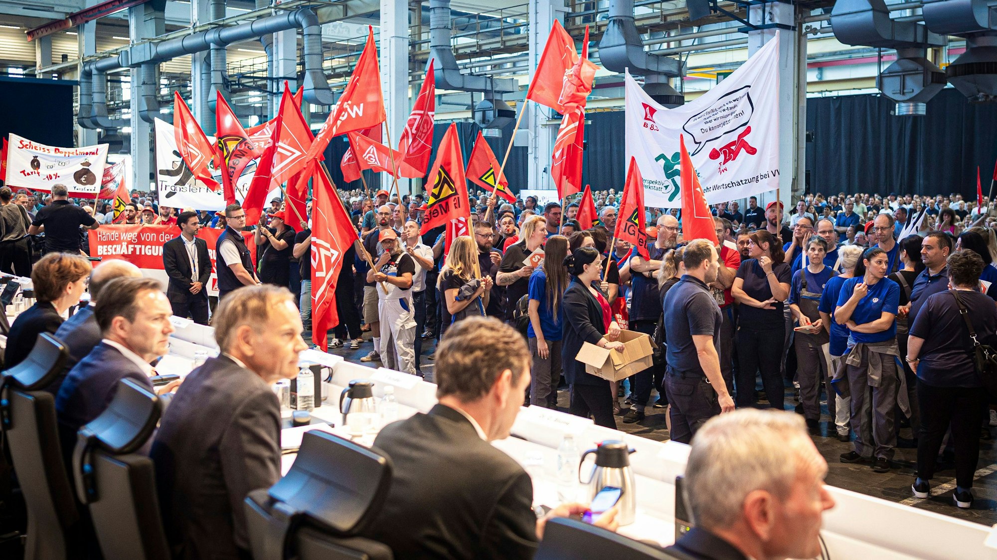 Mitarbeitende protestieren mit Fahnen und Transparenten vor Beginn der Betriebsversammlung von VW.