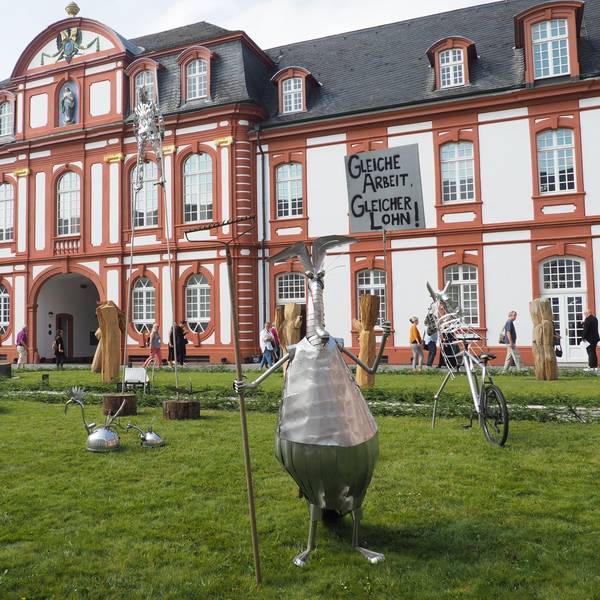 Vor der Abtei in Pulheim-Brauweiler stehen verschiedene kleine Skulpturen aus Blech. Vorne im Bild etwa ein stehender Ameisenbär, der eine Harke hält wie einen Speer.