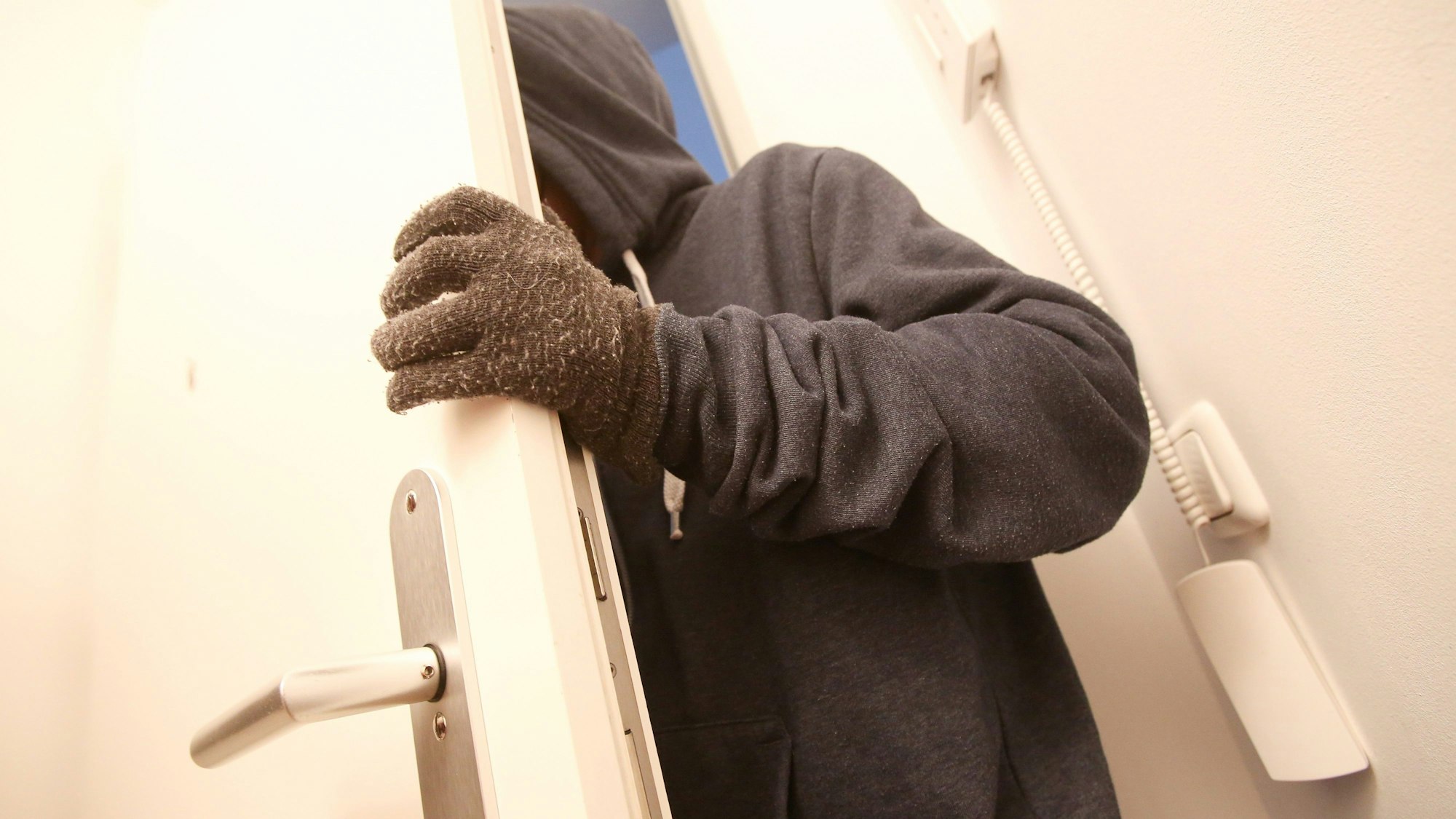 Das Bild zeigt einen vermummten Einbrecher, der durch eine Wohnungstür geht.