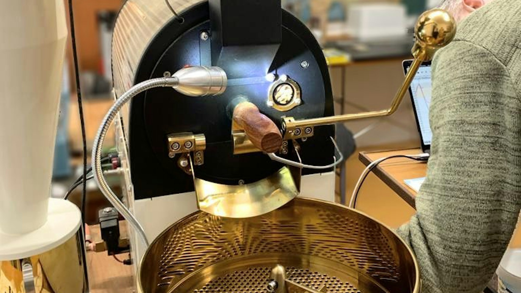 Eine golden-weiße Kaffeeröstmaschine. Daneben eine Person.