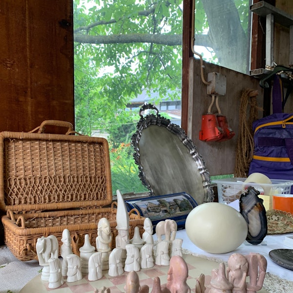 Das Bild zeigt einen Picknickkorb im Hintergrund, im Vordergrund ein Schachset. Daneben liegt ein Straußenei und weitere Gegenstände von einem Trödelmarkt.