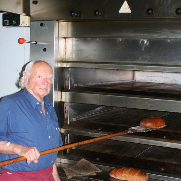 Ein Mann steht am Backofen und holt ein Brot heraus.