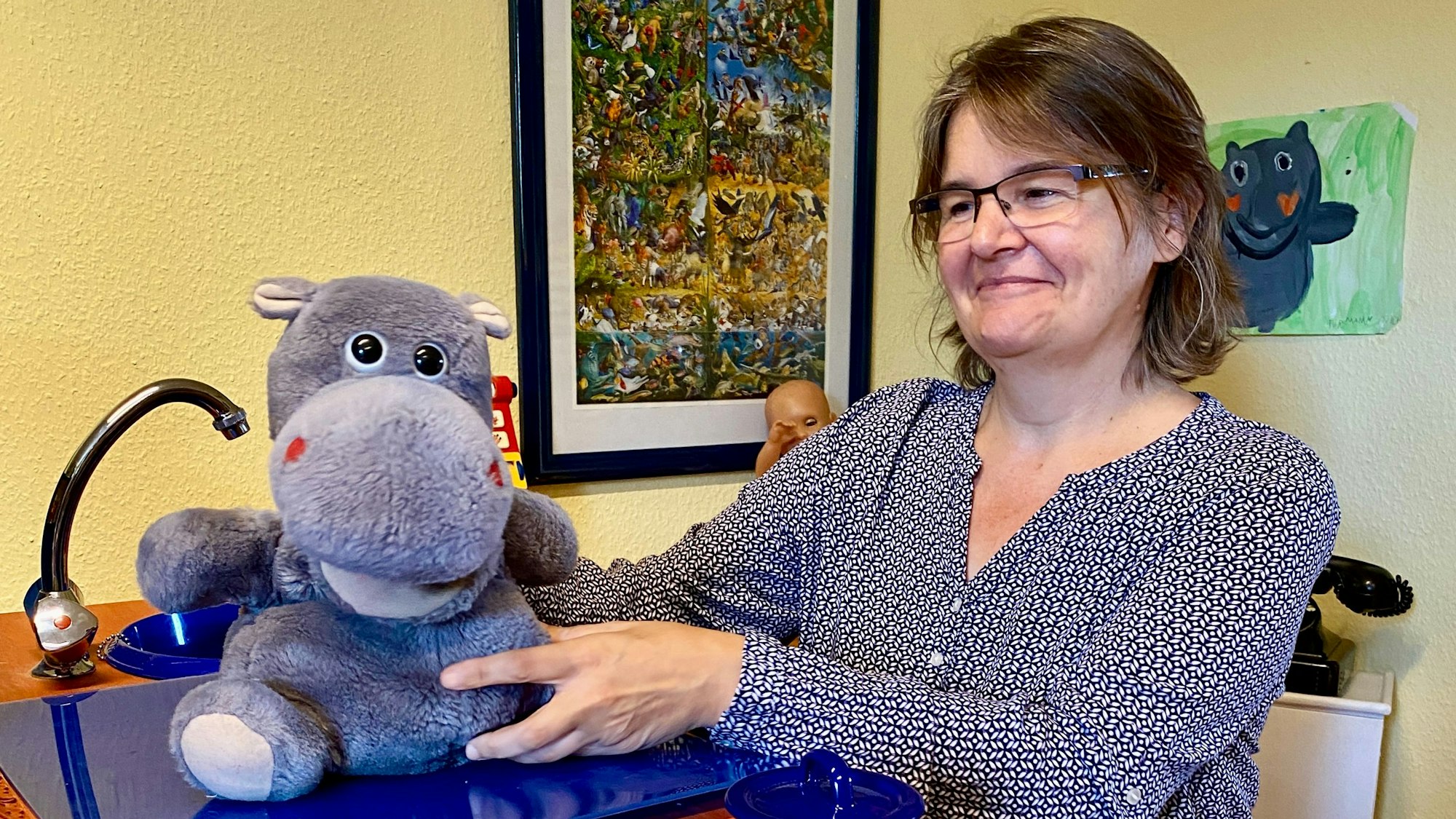 Eine Frau mit Brille fasst ein an eine Nilpferd-Handpuppe, die sich auf einem Schreibtisch befindet.