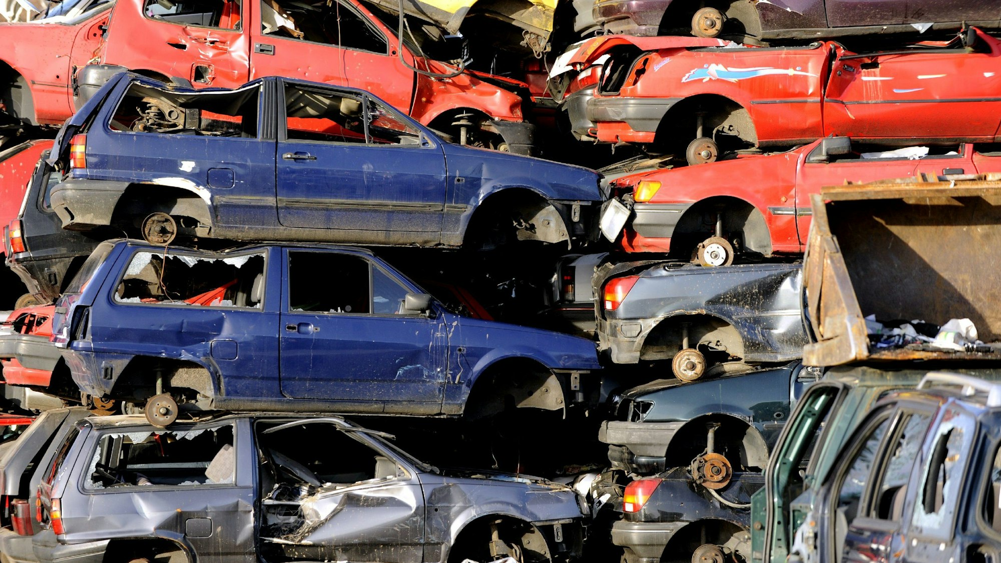 Das Foto zeigt aufeinander gestapelte Autos auf einem Schrottplatz.