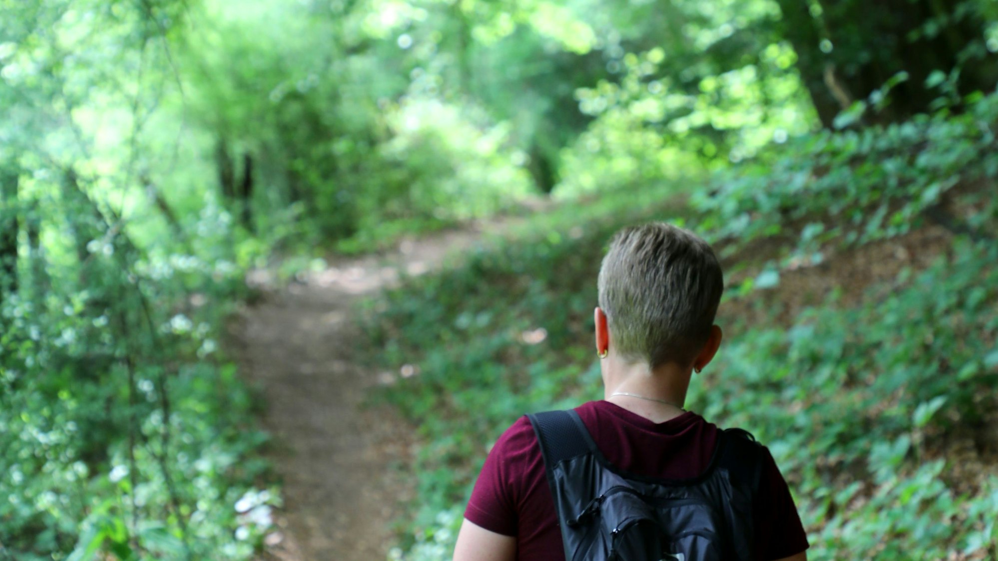 Eine Frau geht auf einem schattigen Pfad durch den Wald.