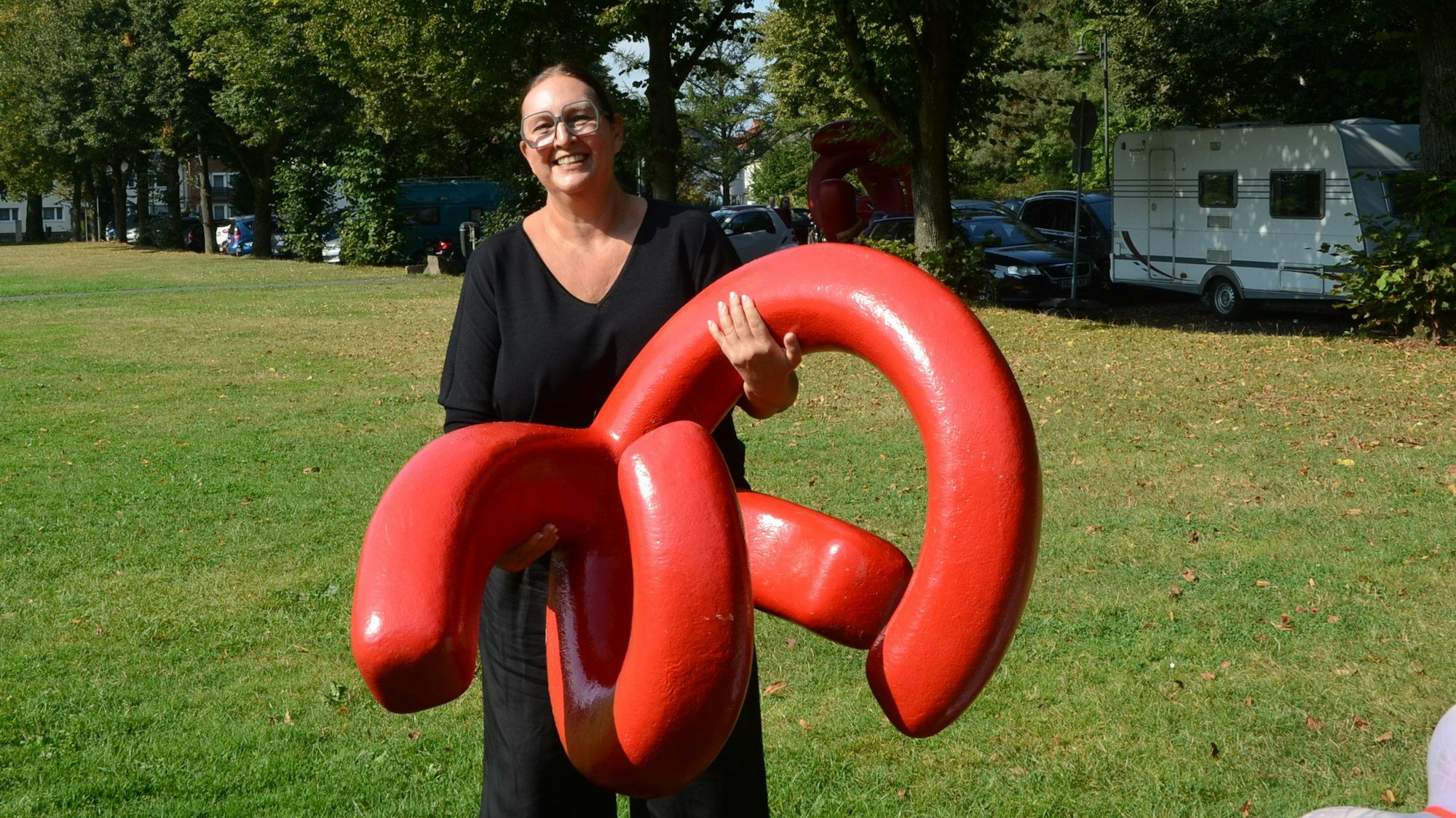 Eine Frau in schwarzer Kleidung trägt eine moderne rote Skulptur.