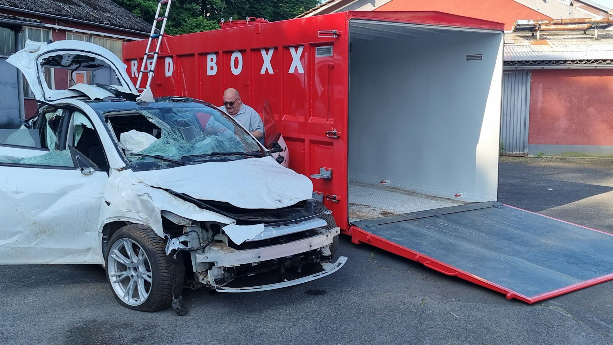 Ein Schrottauto steht neben einem offenen Container.