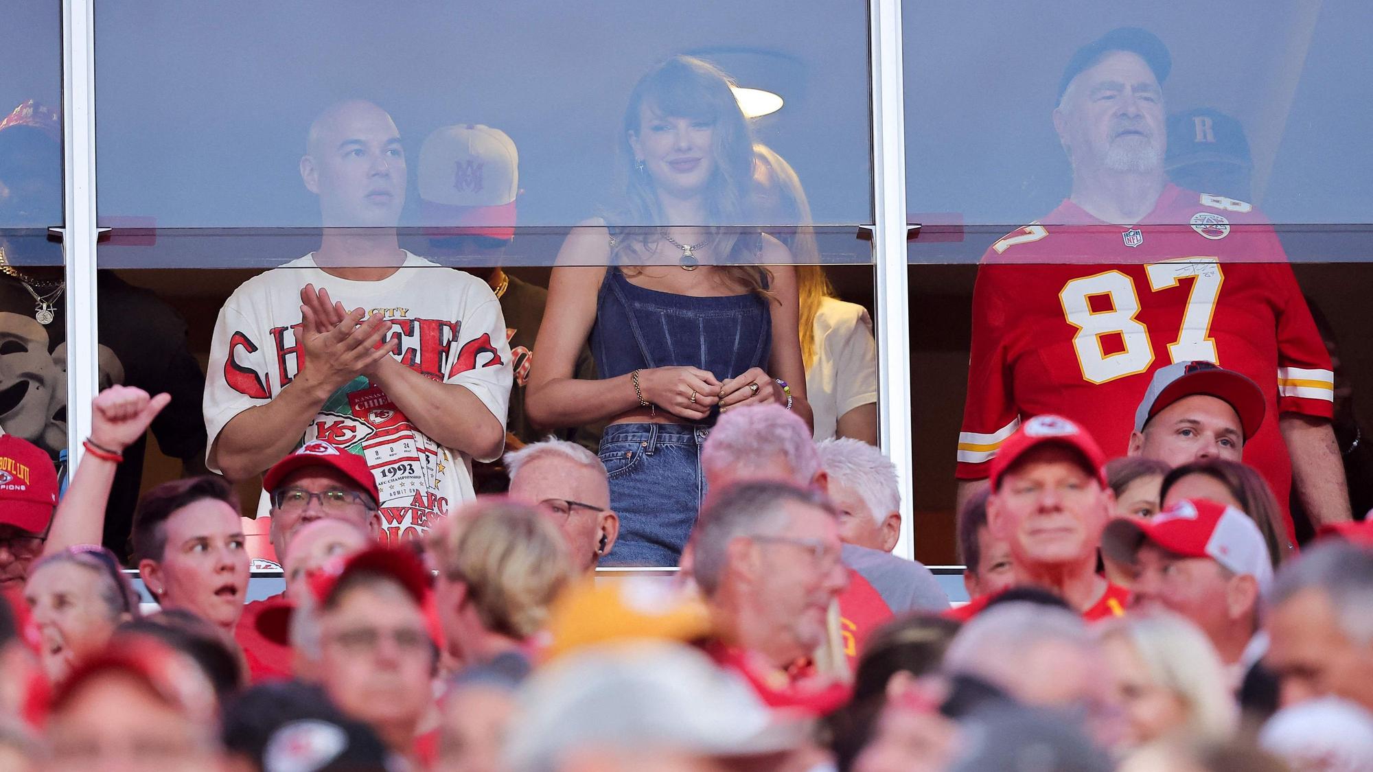 Taylor Swift steht in einer Loge und schaut ein Football-Spiel.