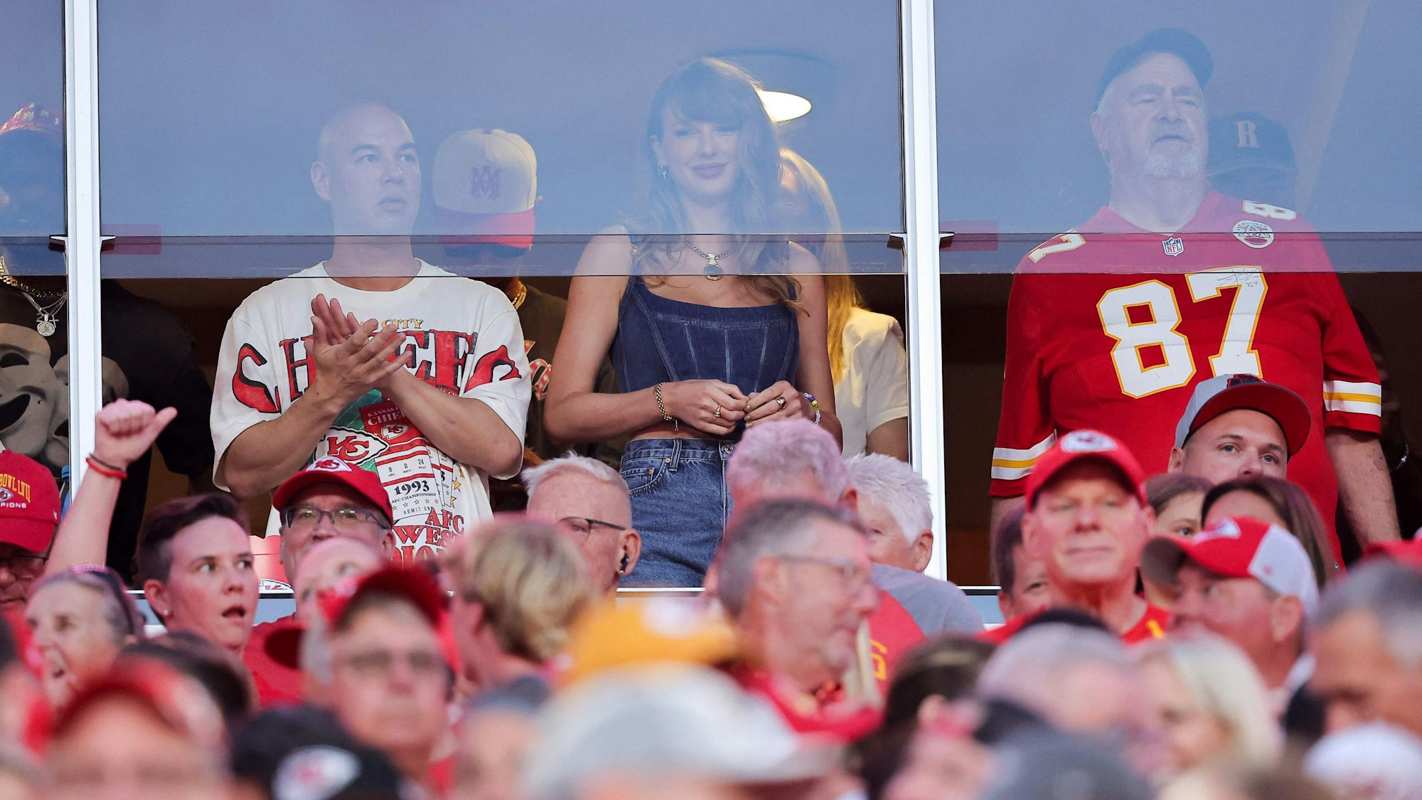 Taylor Swift steht in einer Loge und schaut ein Football-Spiel.