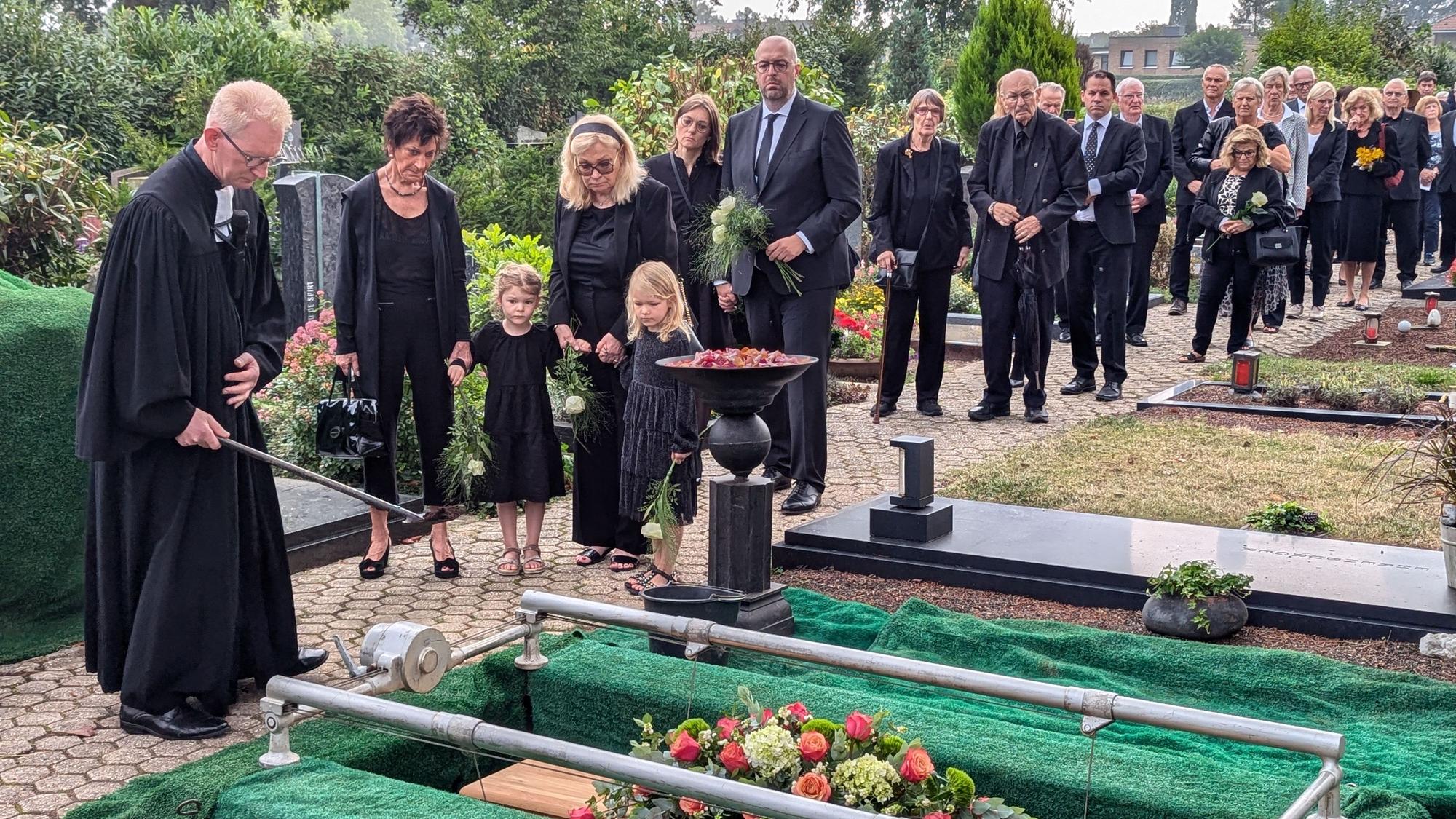 Das Foto zeigt den Pfarrer und die Familie am offenen Grab, dahinter ein langer Trauerzug.