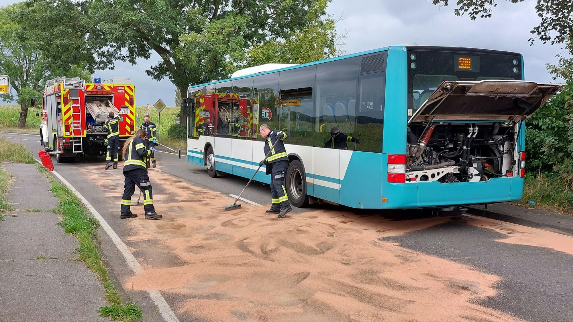 Feuerwehrleute fegen neben einem Linienbus.