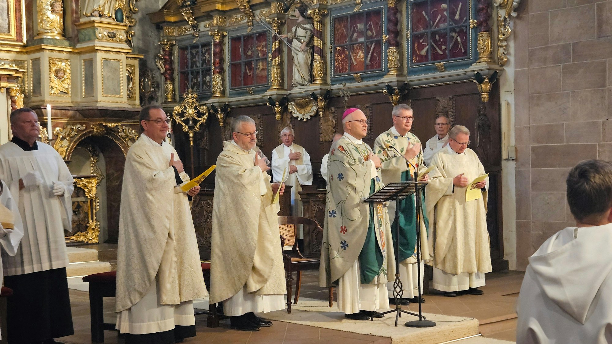 Bischof Helmut Dieser steht am Rednerpult, weitere Geistliche stehen links und rechts von ihm.