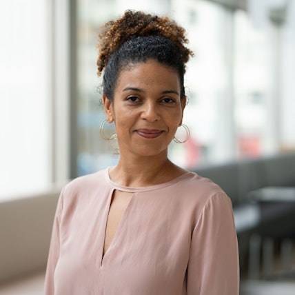 Jackie Thomae trägt eine rosafarbene Bluse und lächelt in die Kamera.