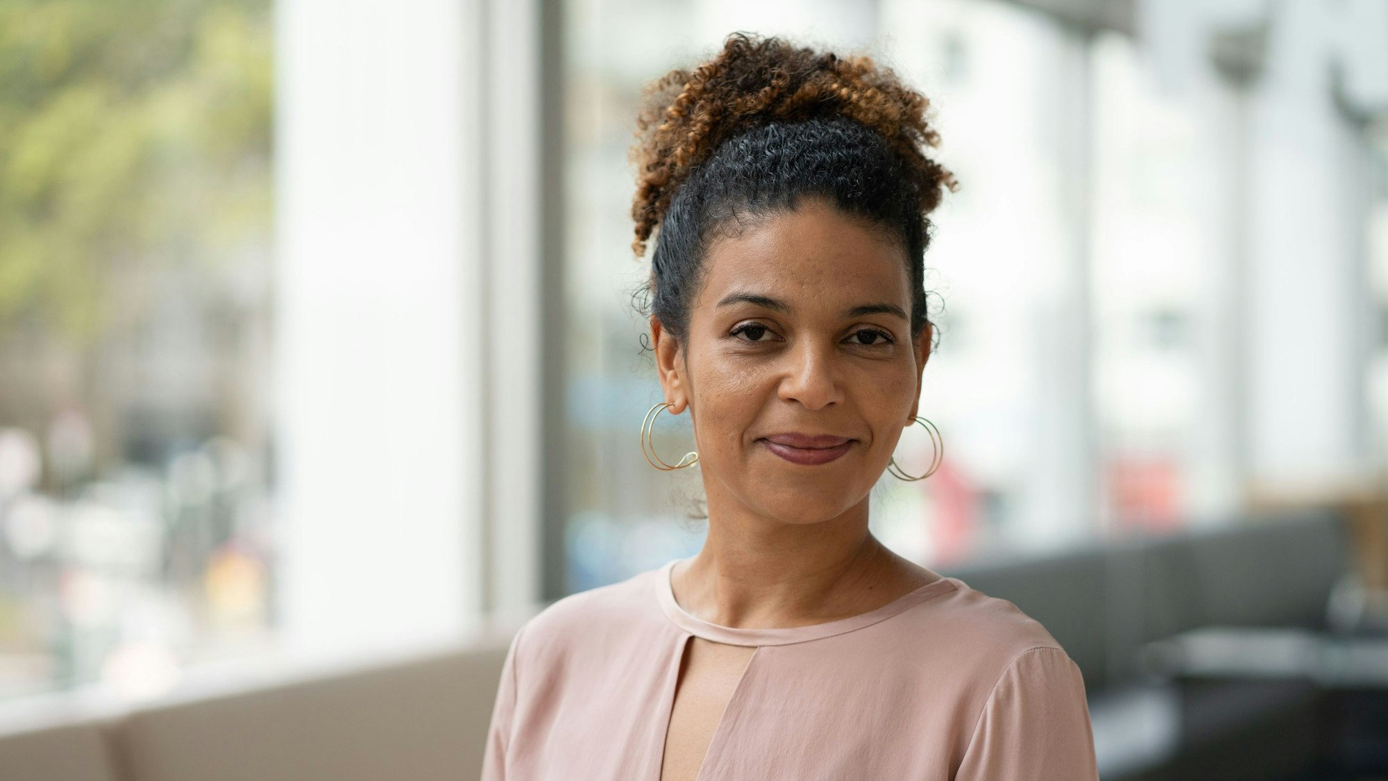 Jackie Thomae trägt eine rosafarbene Bluse und lächelt in die Kamera.