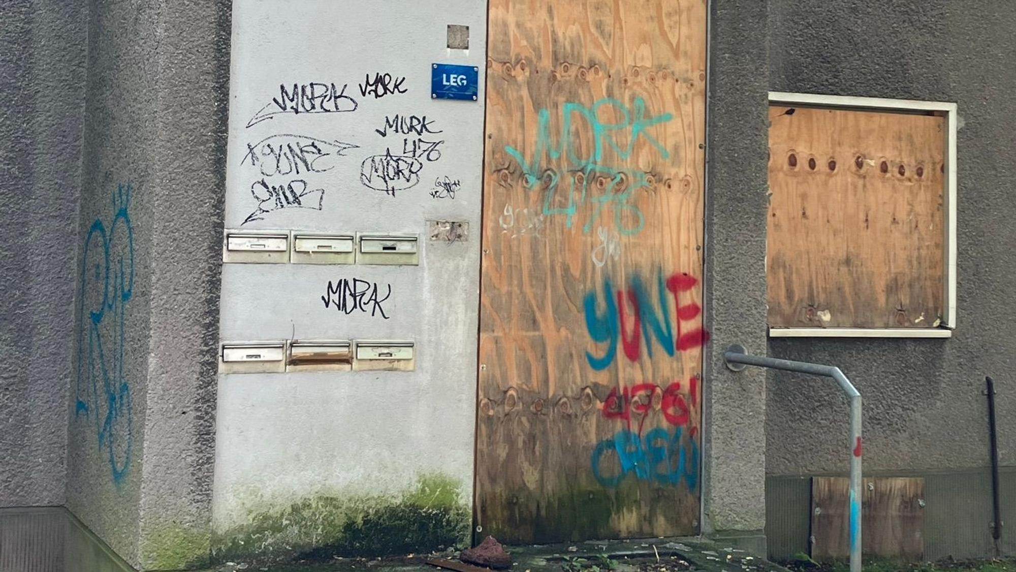 Zu sehen sind verbretterte Fenster und Türen sowie Graffiti-Beschmierungen an den Wohnhäusern um den Schlebuscher Weg.