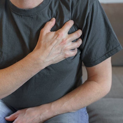 Ein Mann sitzt auf einem Sofa und hält sich die Brust