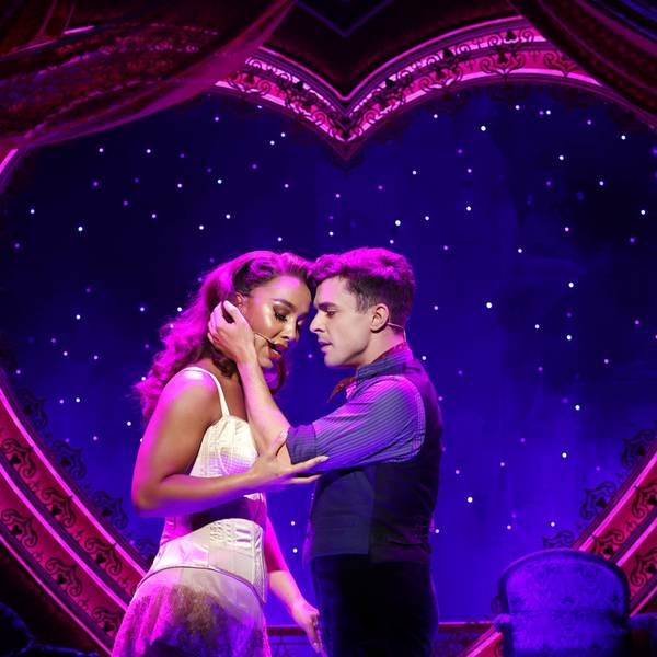 Musicaldarsteller von Moulin Rouge halten sich aneinander fest und singen, im Hintergrund ein Herz und viele kleine Lichter.
