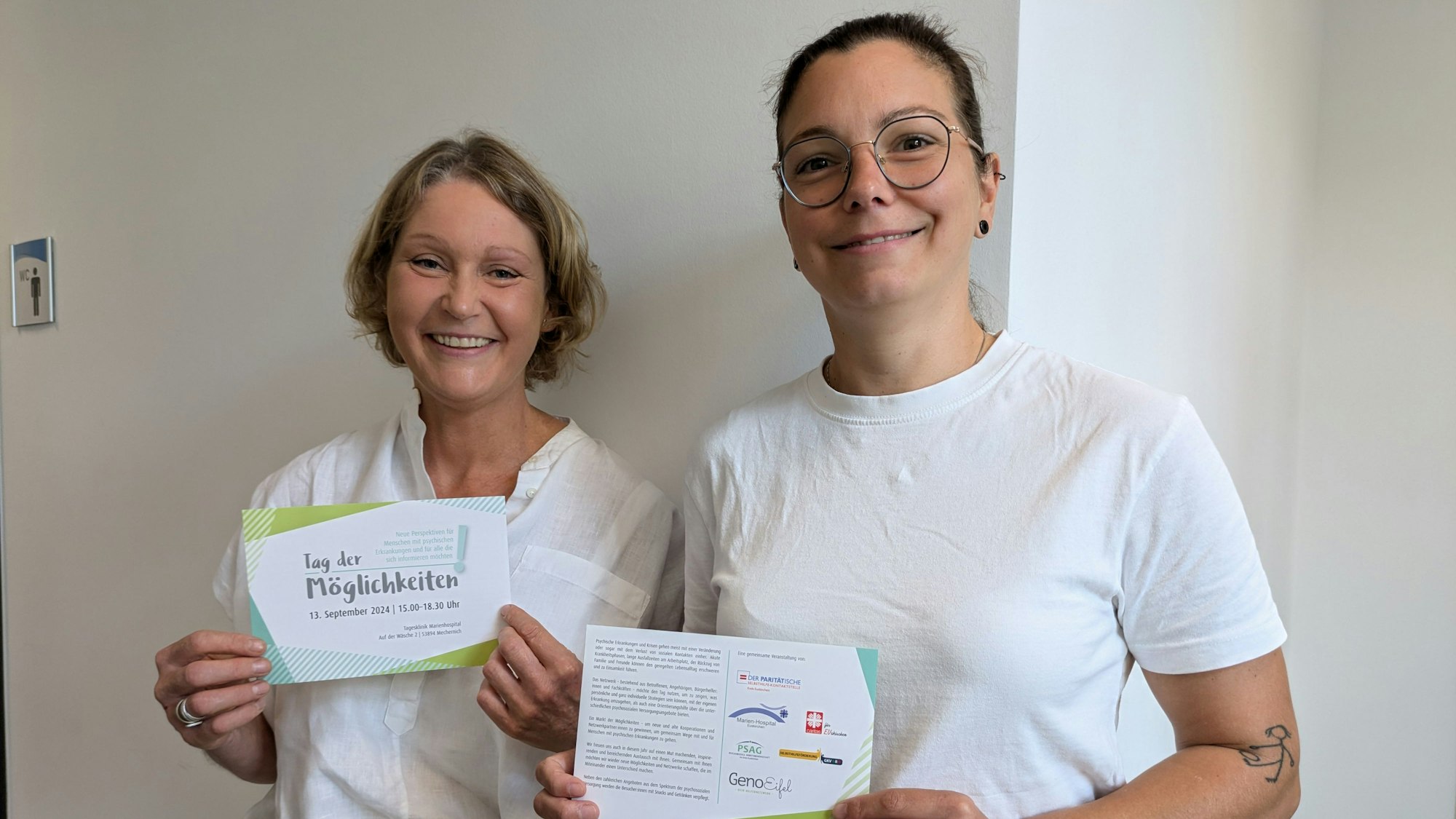 Zwei Frauen halten fröhlich Flyer zum „Tag der Möglichkeiten“ in die Kamera.