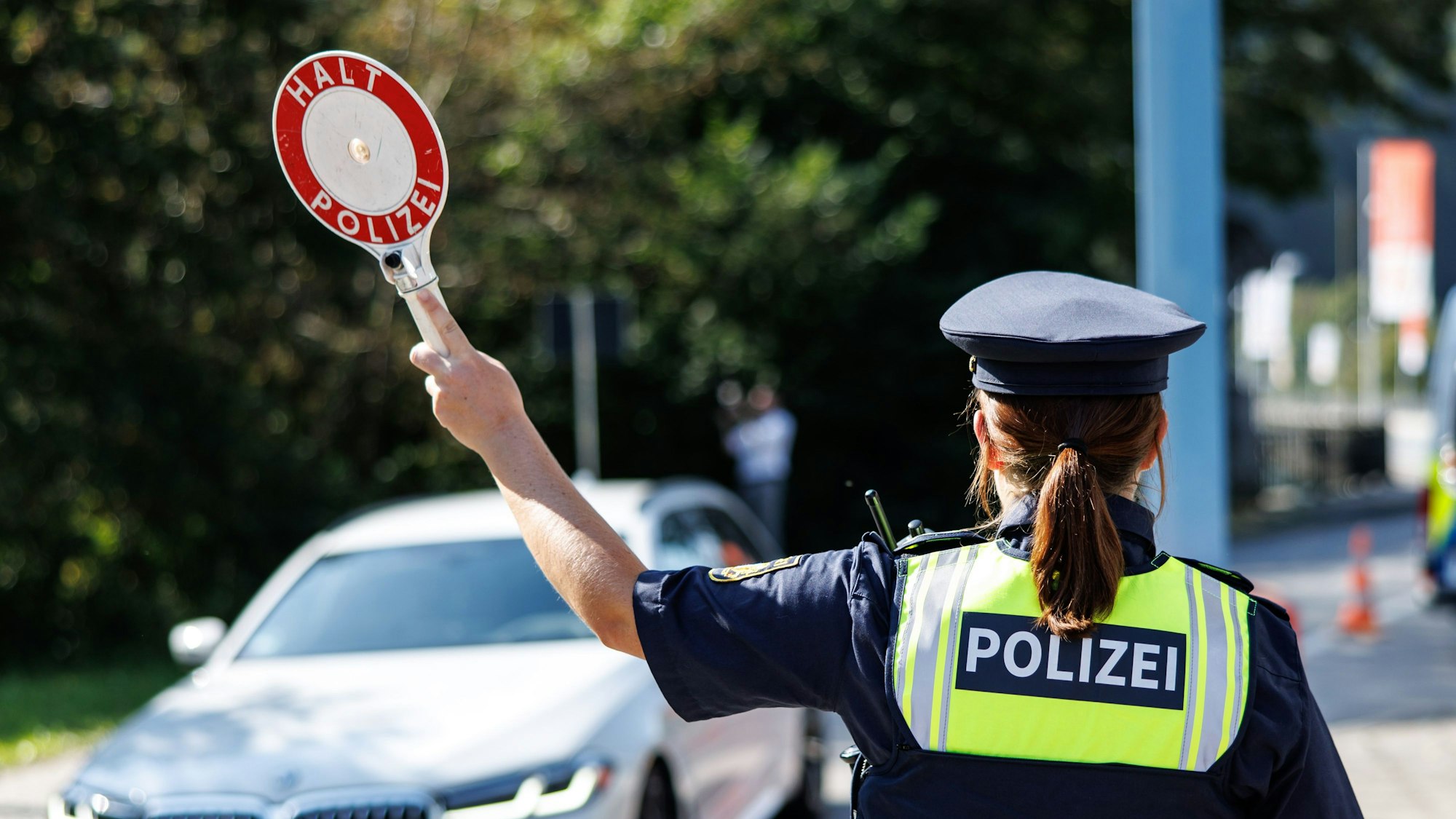 05.09.2024, Bayern, Burghausen: Eine Polizistin der Bayerischen Grenzpolizei stoppt bei einem Pressetermin an einer Kontrollstelle ein Fahrzeug.