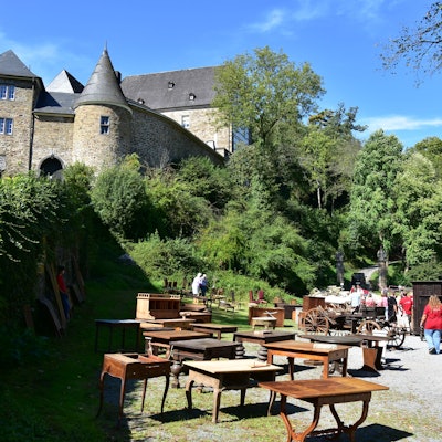 Eine alte Burg, auf einem Schotterplatz im Vordergrund stehen alte Möbel.