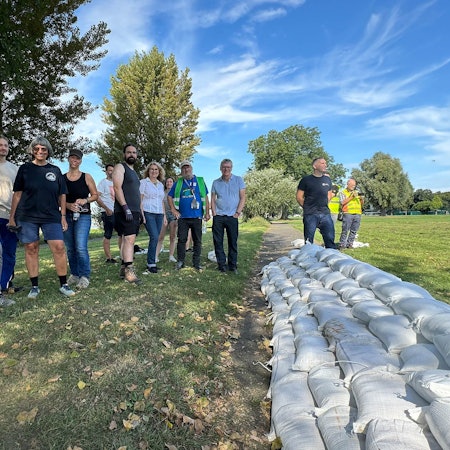 Freiwillige Helferinnen und Helfer vor dem von ihnen aufgebauten Sandsackwall am Samstag am Rheinufer in Köln-Poll.