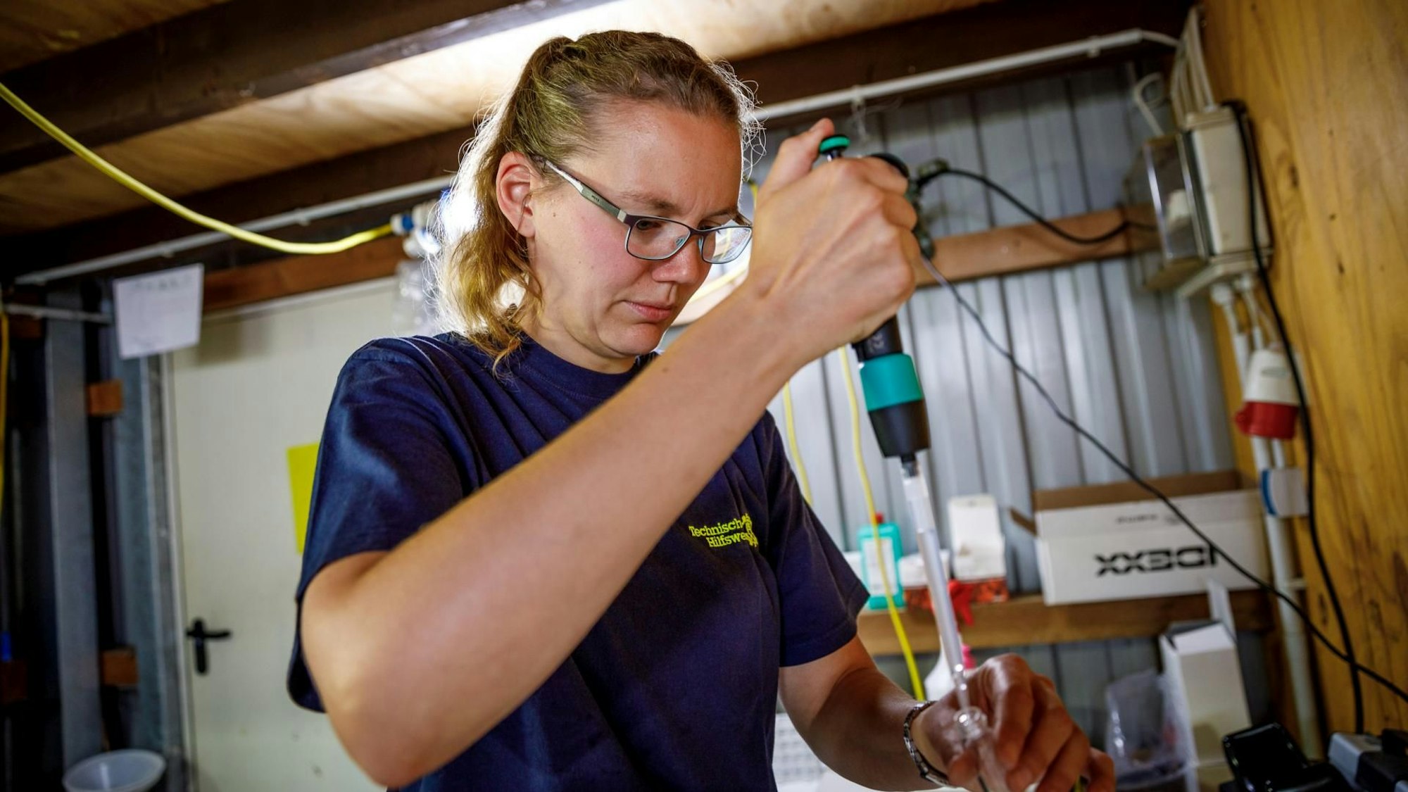 Eine Frau in einem dunkelblauen T-Shirt füllt mit einer Pipette Wasser in ein kleines Glas.