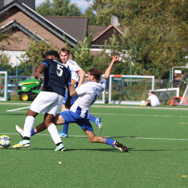 Ein Zweikampf, in dem ein Spieler mit gestrecktem Bein den Ball vor dem Gegner wegspitzelt.