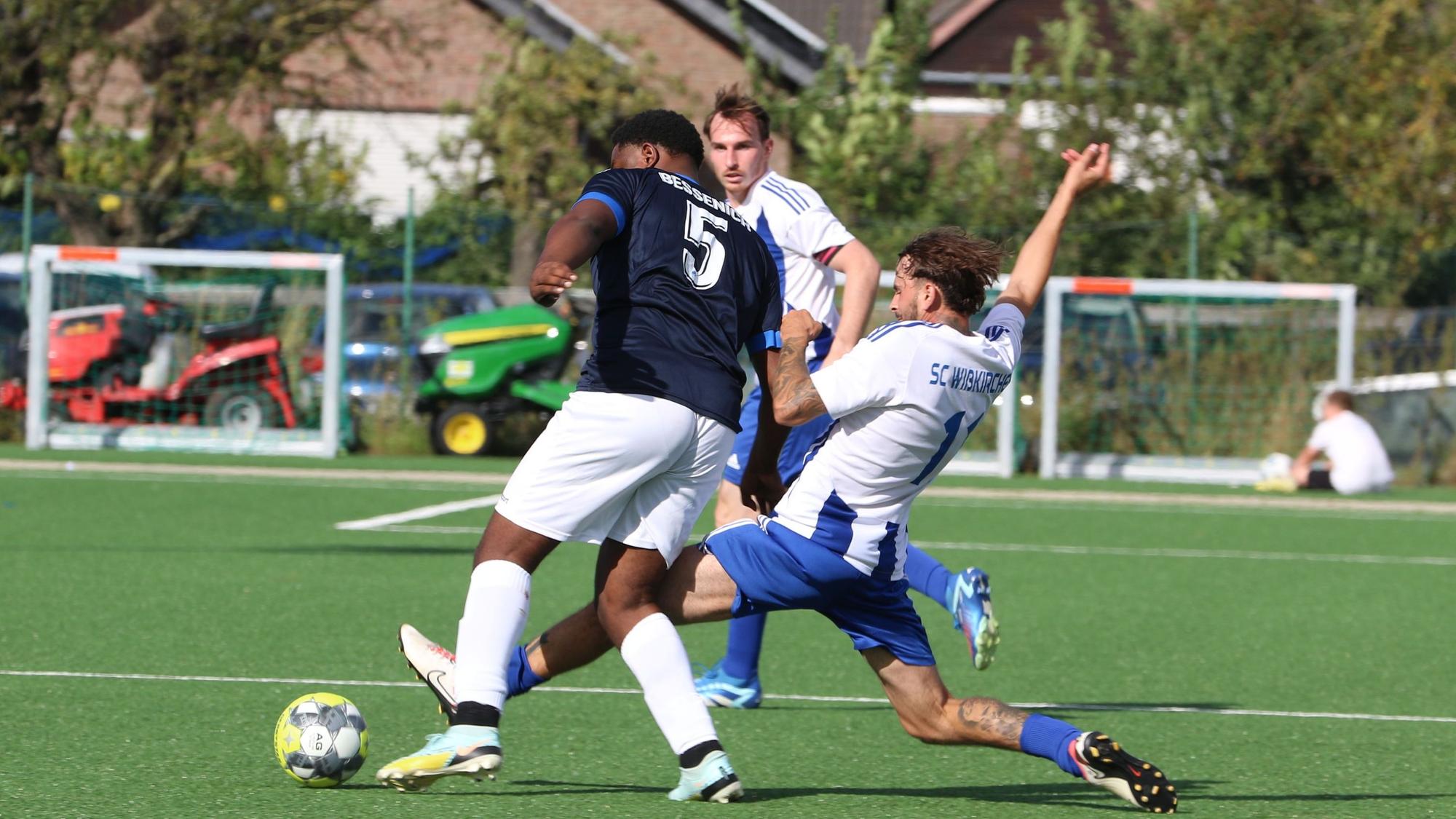 Ein Zweikampf, in dem ein Spieler mit gestrecktem Bein den Ball vor dem Gegner wegspitzelt.
