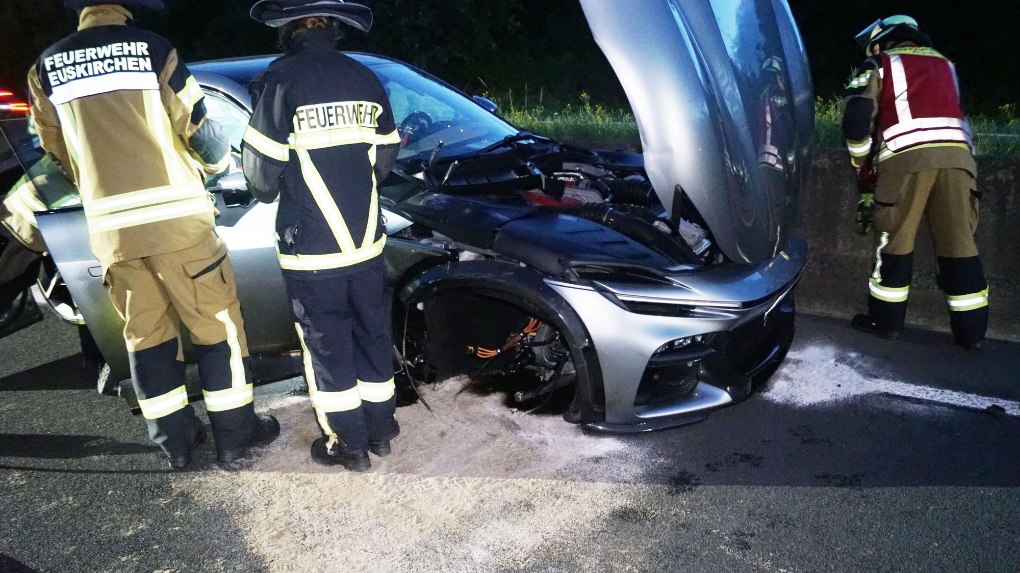 Feuerwehrleute stehen um einen zerstörten silbernen Ferrari.