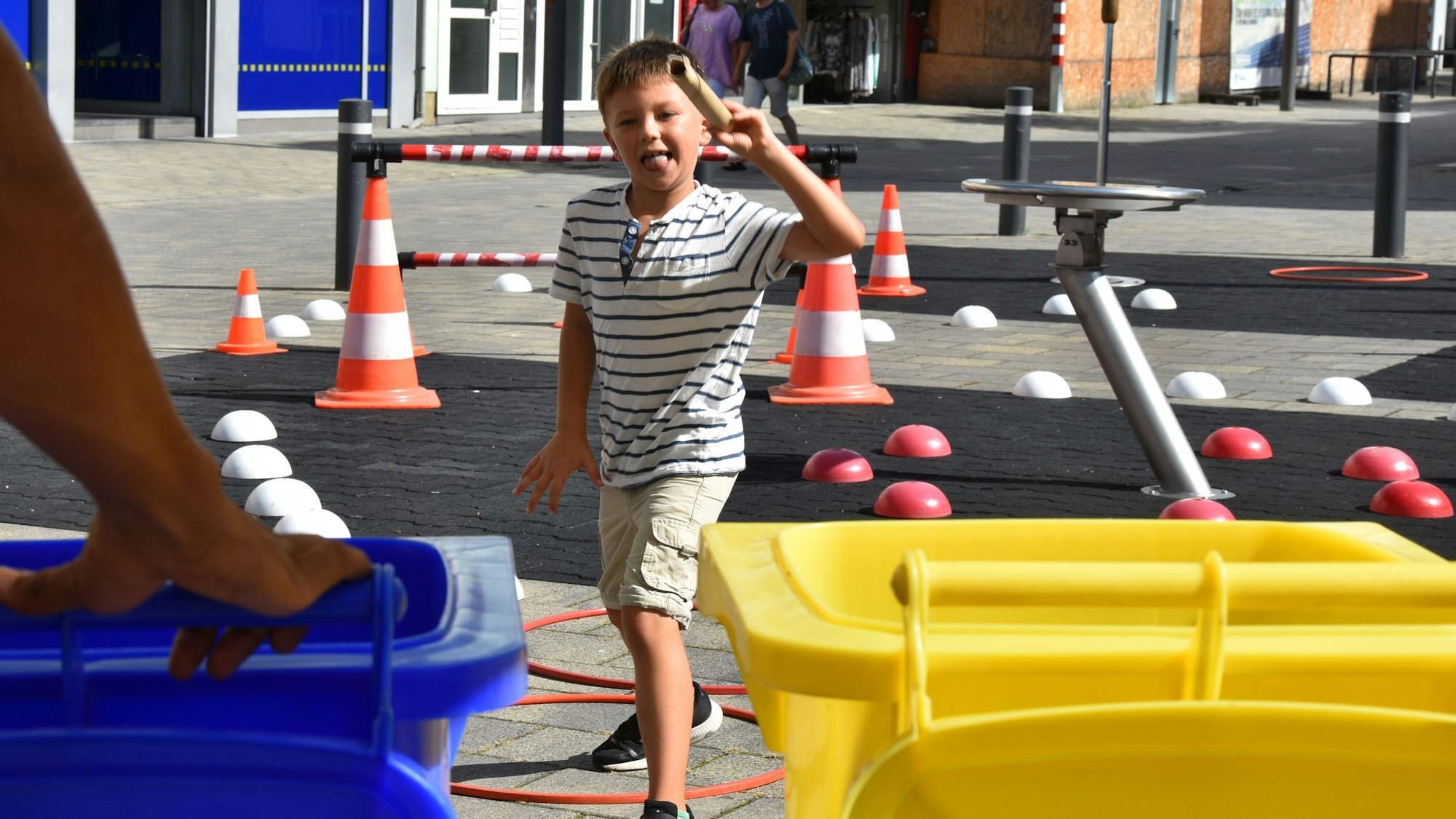 Ein Junge läuft durch einen Parcours aus kleinen Pylonen auf zwei Mülltonnen zu.