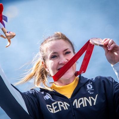 Edina Müller jubelt nach dem Rennen mit ihrer Bronzemedaille und hält Phryges, das Maskottchen der Paralympics, in ihrer Hand.
