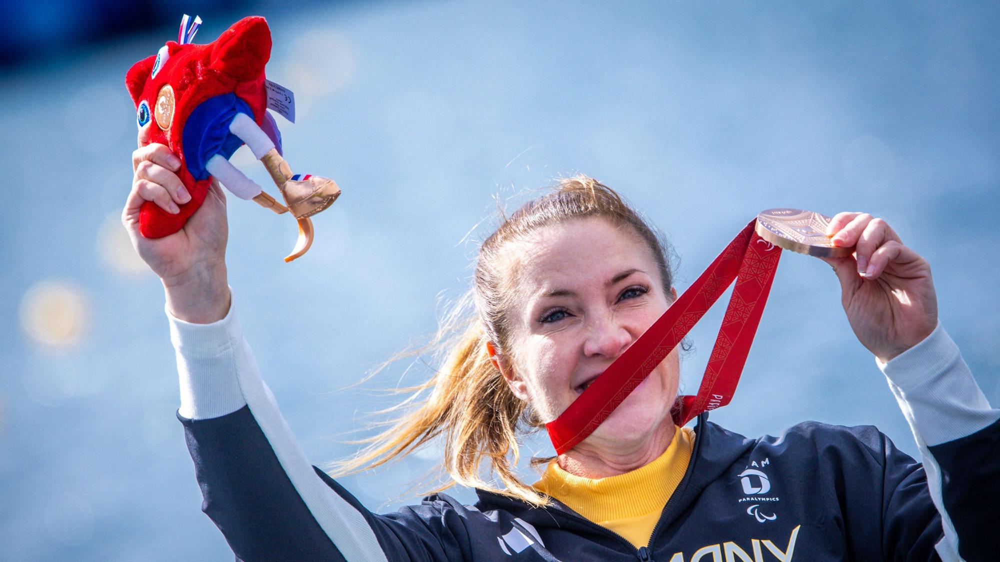 Edina Müller jubelt nach dem Rennen mit ihrer Bronzemedaille und hält Phryges, das Maskottchen der Paralympics, in ihrer Hand.