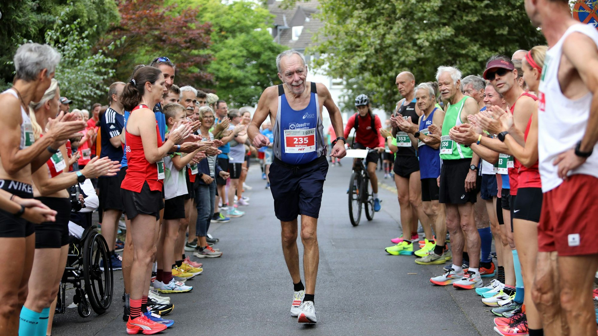 Ein Straßenläufer läuft durch ein Spalier von Männern und Frauen im Laufdress.