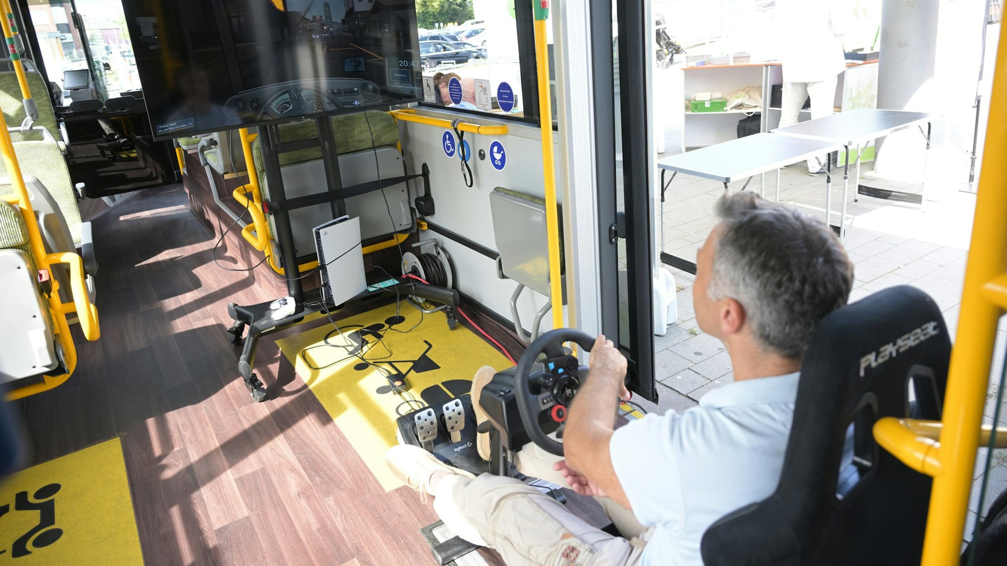 Ein Mann sitzt am Lenkrad eines Busses. Das Gefährt ist aber ein Fahrsimulator.