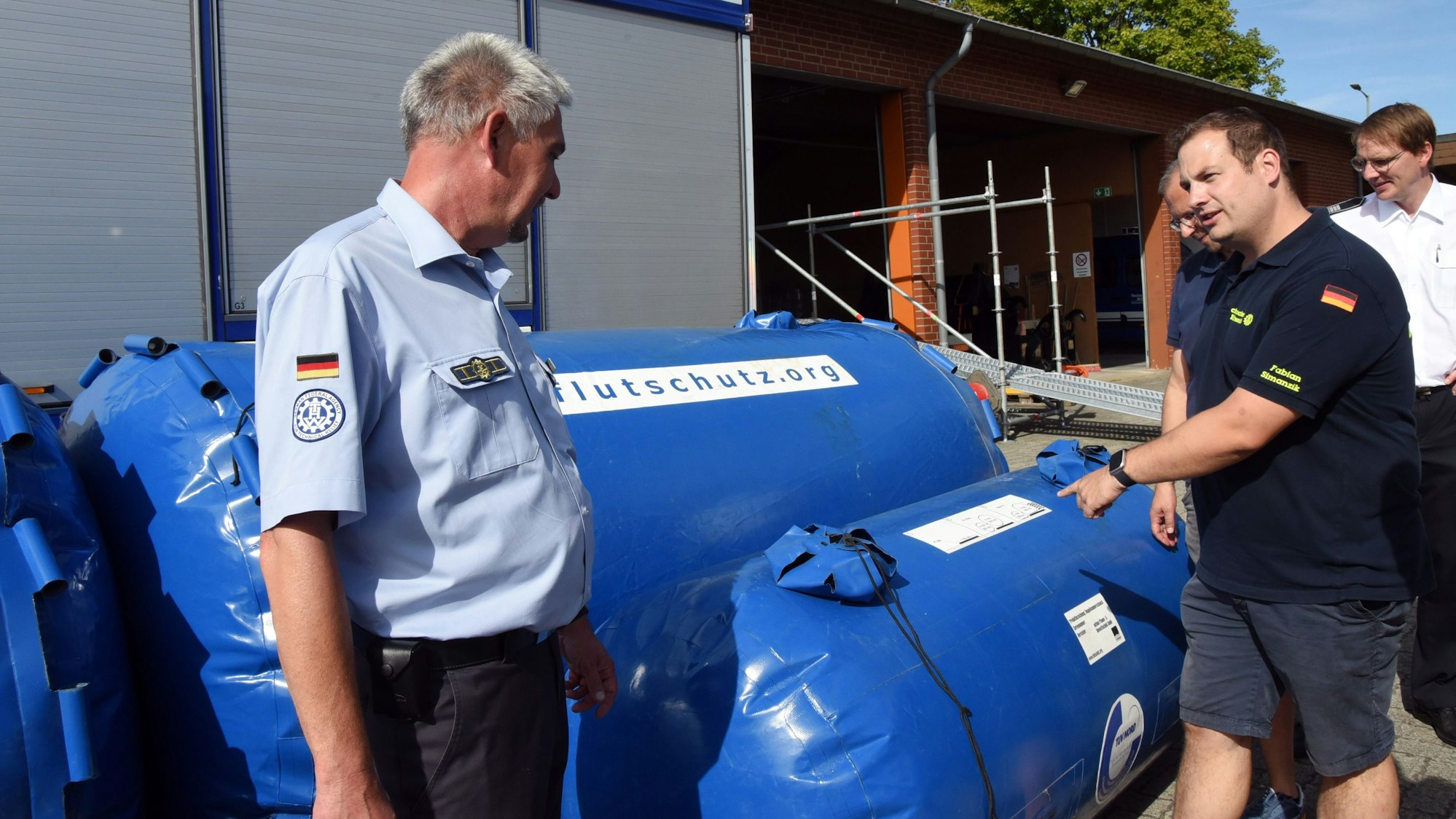 Mit solchen Rollen stoppt das Technische Hilfswerk Flutwasser. Torsten Simon (links), Ortsbeauftragter des THW für Gummersbach, erklärt, wie diese mobilen Barrieren funktionieren.