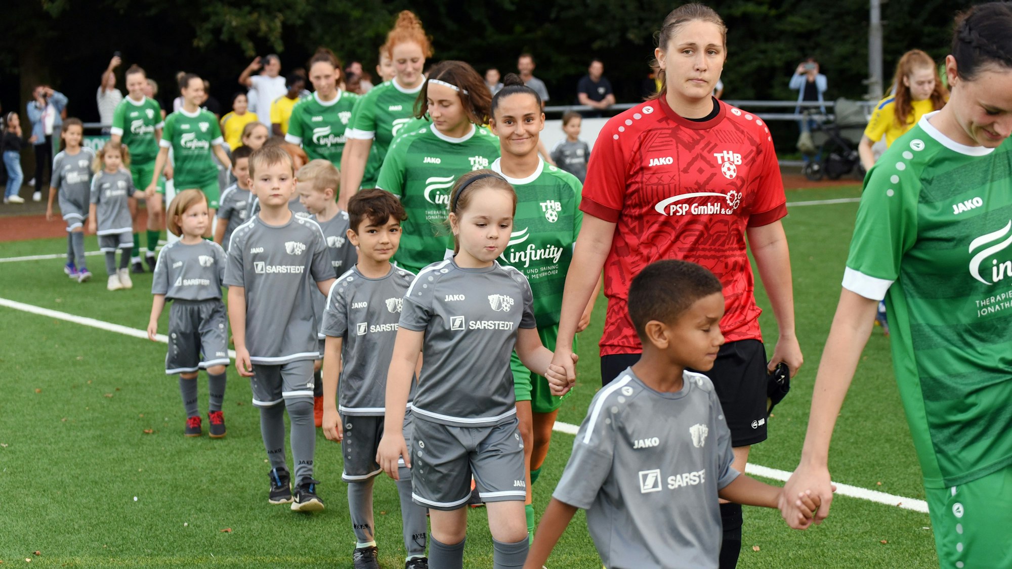 Die Fußballerinnen des TuS Homburg-Bröltal laufen mit Einlaufkindern an den Händen ins Stadion ein.