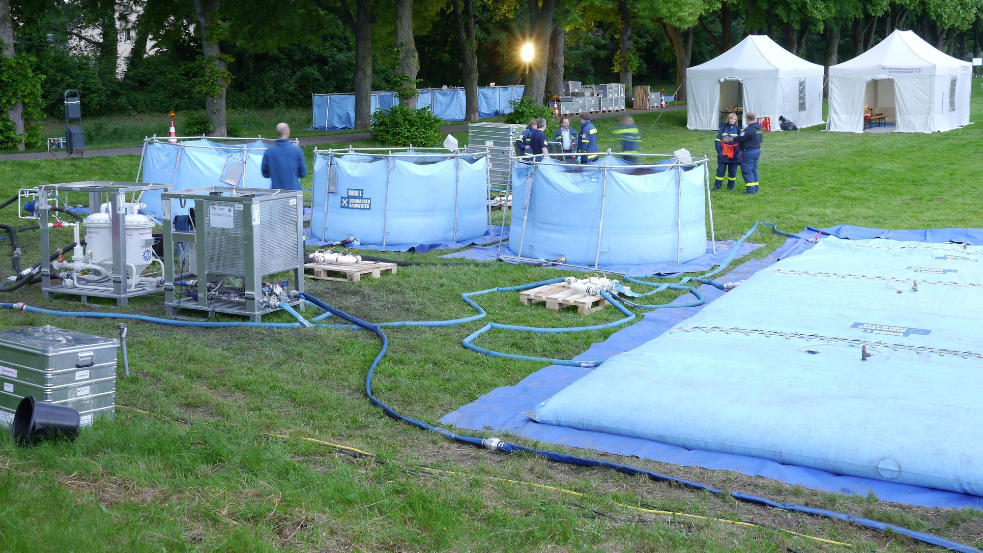 Mehrere Schläuche verbinden unterschiedliche hellblaue Becken, die auf einer Wiese stehen.