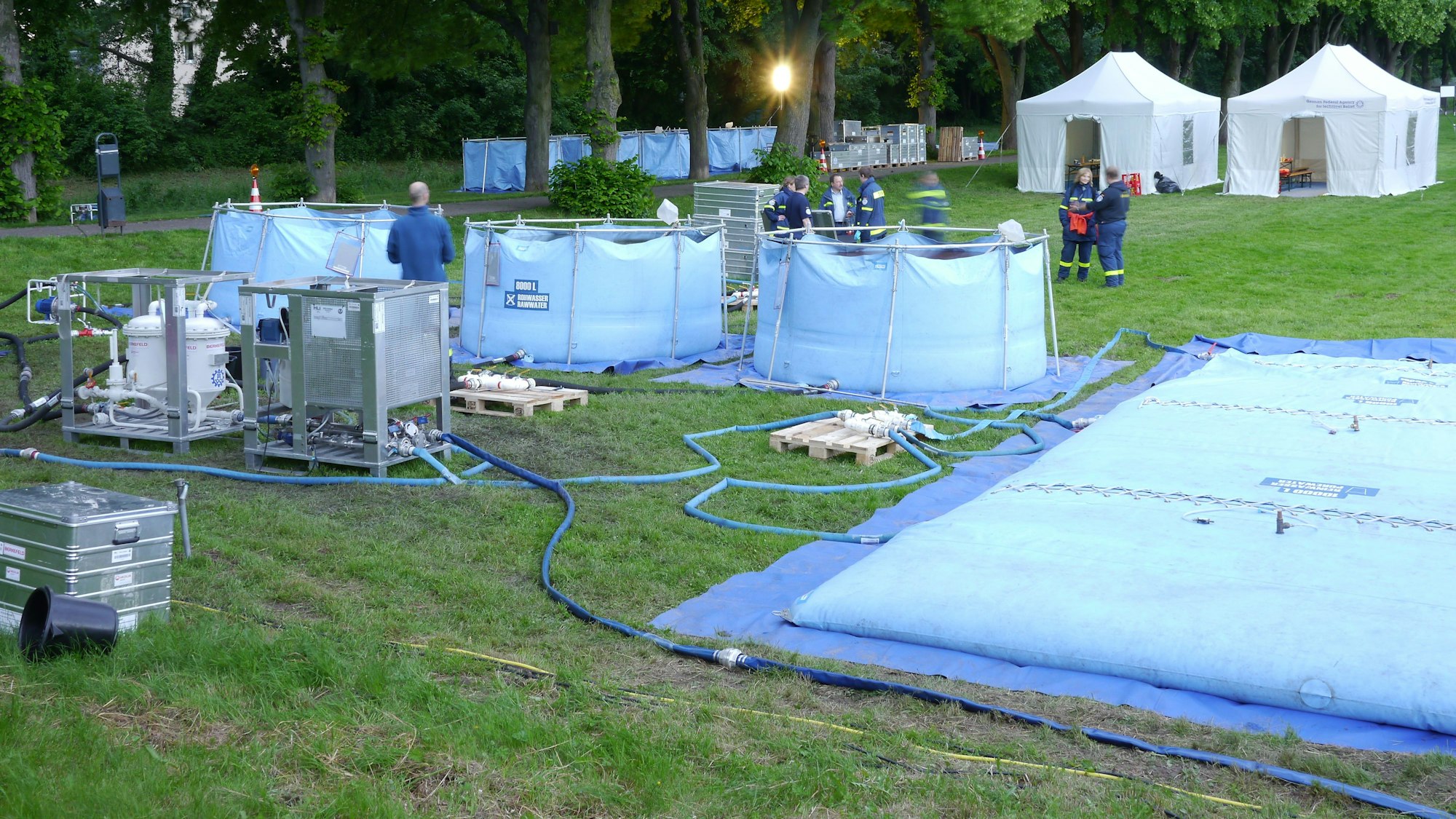 Mehrere Schläuche verbinden unterschiedliche hellblaue Becken, die auf einer Wiese stehen.