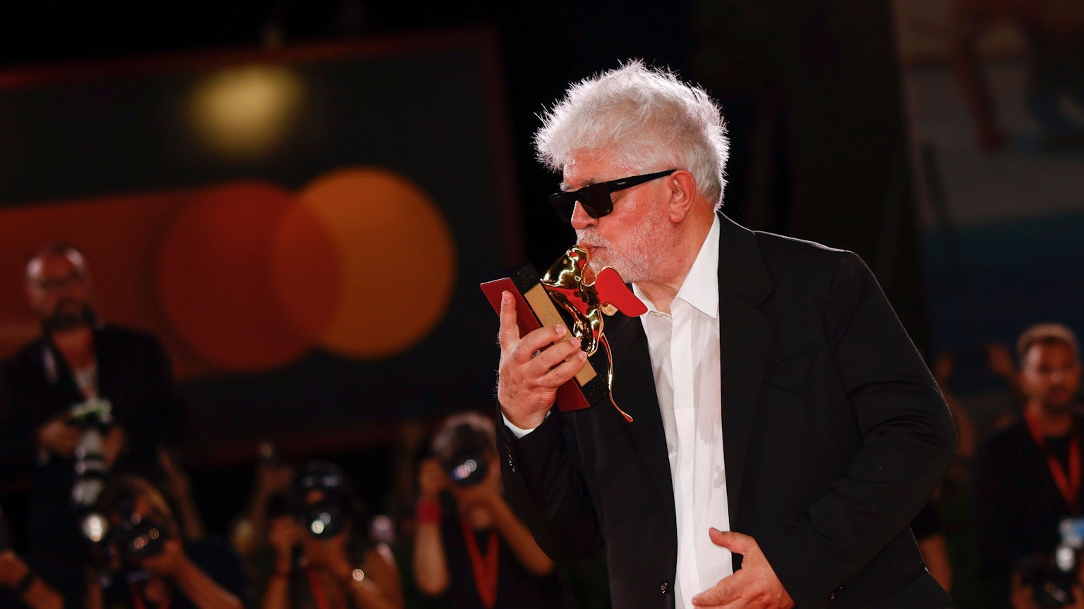 Pedro Almodóvar steht in einem schwarzen Anzug vor Fotografen und küsst den Goldenen Löwen, den er gewonnen hat