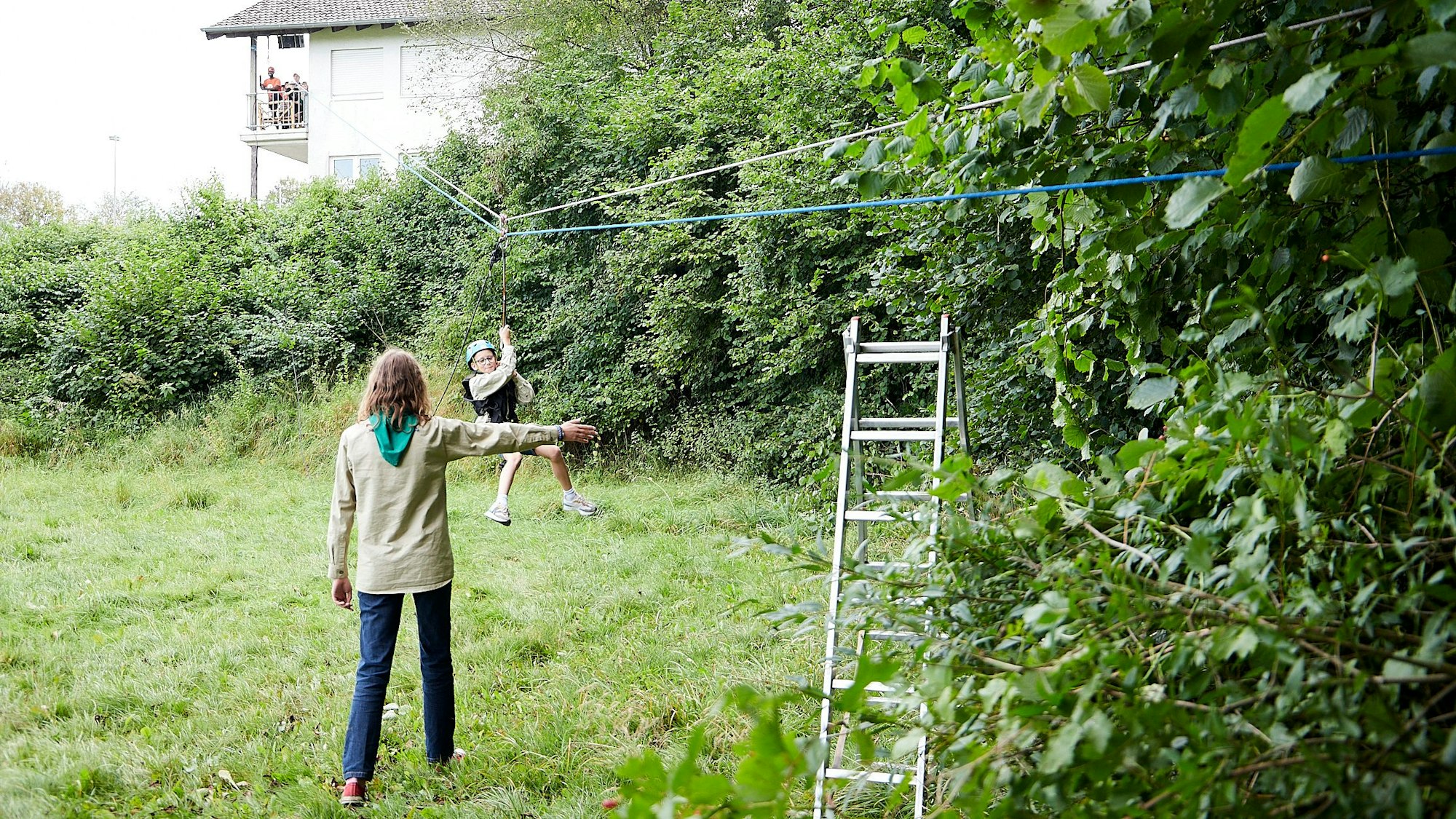 Ein Kind rutscht an einer Seilrutsche zwischen Hecken herunter. Ein Pfadfinder passt auf, dass nichts passiert.