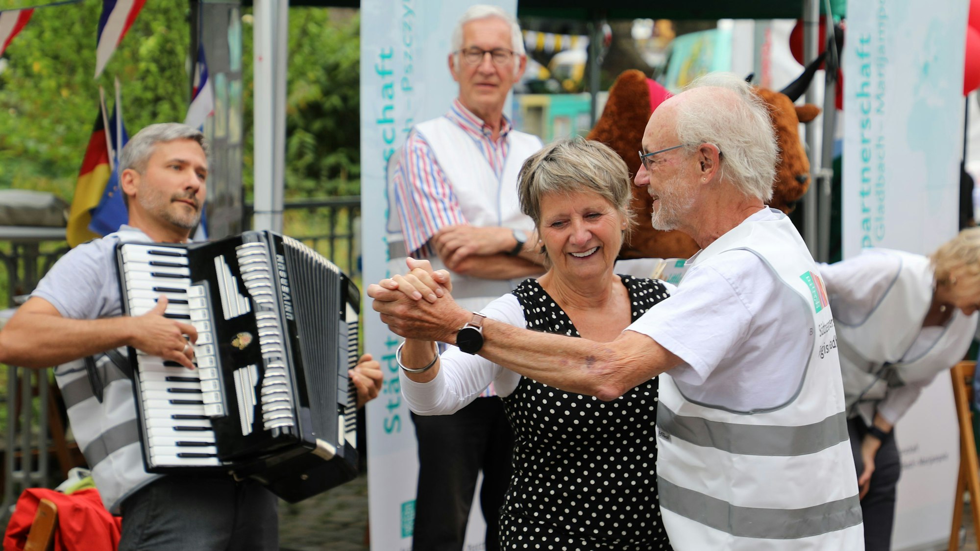 Ein Paar tanzt, ein Mann spielt Akkordeon an den Ständen der Partnerschaftsverein auf dem Bergisch Gladbacher Stadtfest.