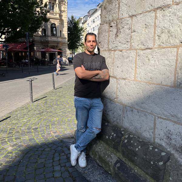 Siavash Hosseini lehnt an einer Mauer der Eigelsteintorburg. Die Arme sind verschränkt, der Blick zuversichtlich.