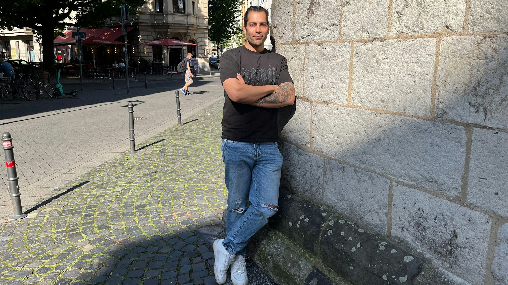 Siavash Hosseini lehnt an einer Mauer der Eigelsteintorburg. Die Arme sind verschränkt, der Blick zuversichtlich.