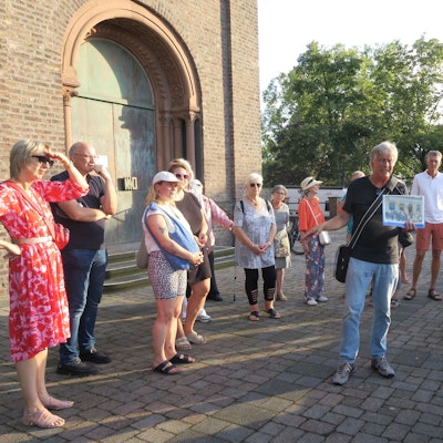 Zu sehen sind Besucher einer Führung vor dem Haupteingang von St. Rochus.