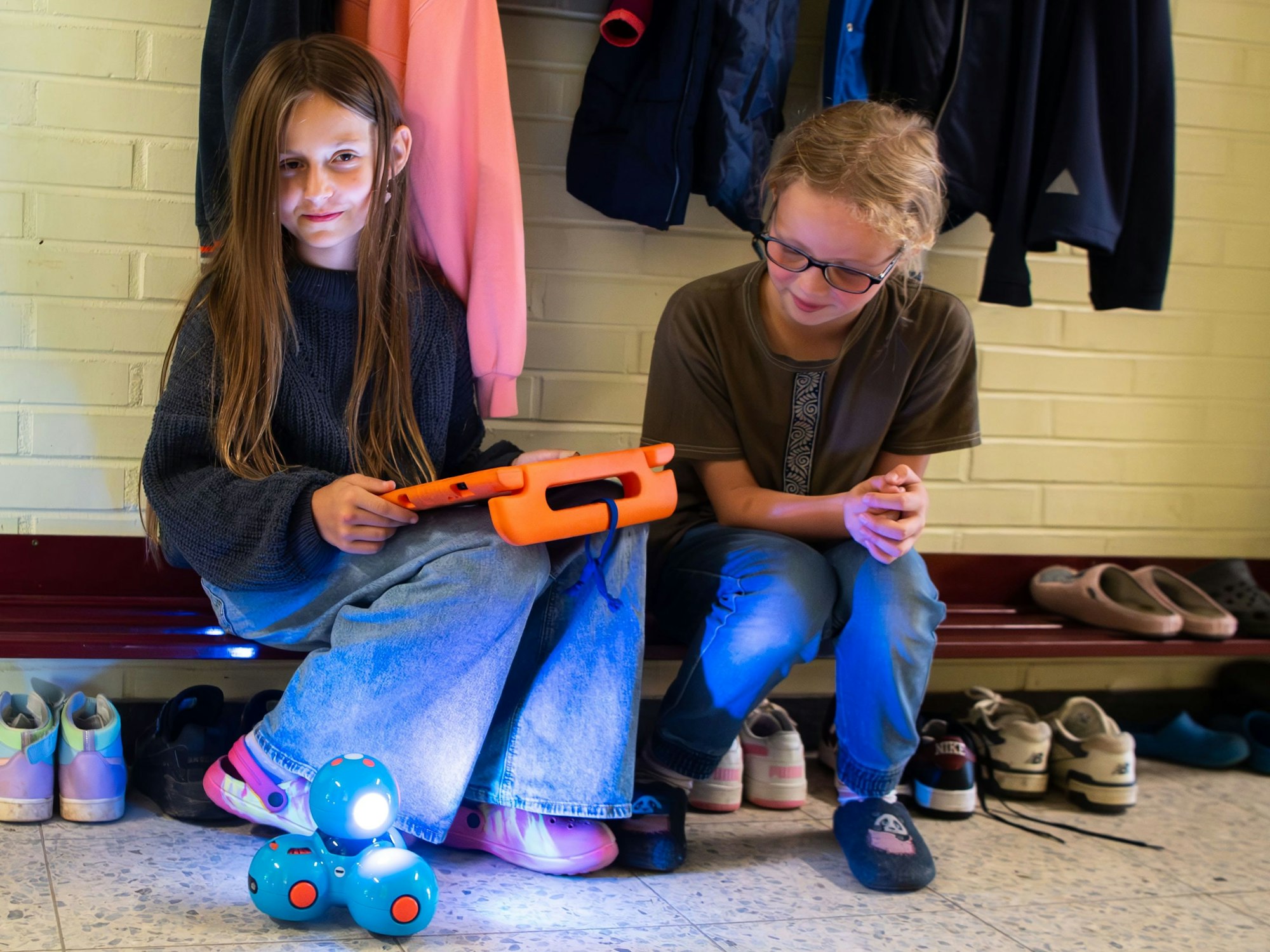 Zwei Grundschülerinnen sitzen in einem Gang, wobei eine der beiden einen Roboter mittels iPad steuert.
