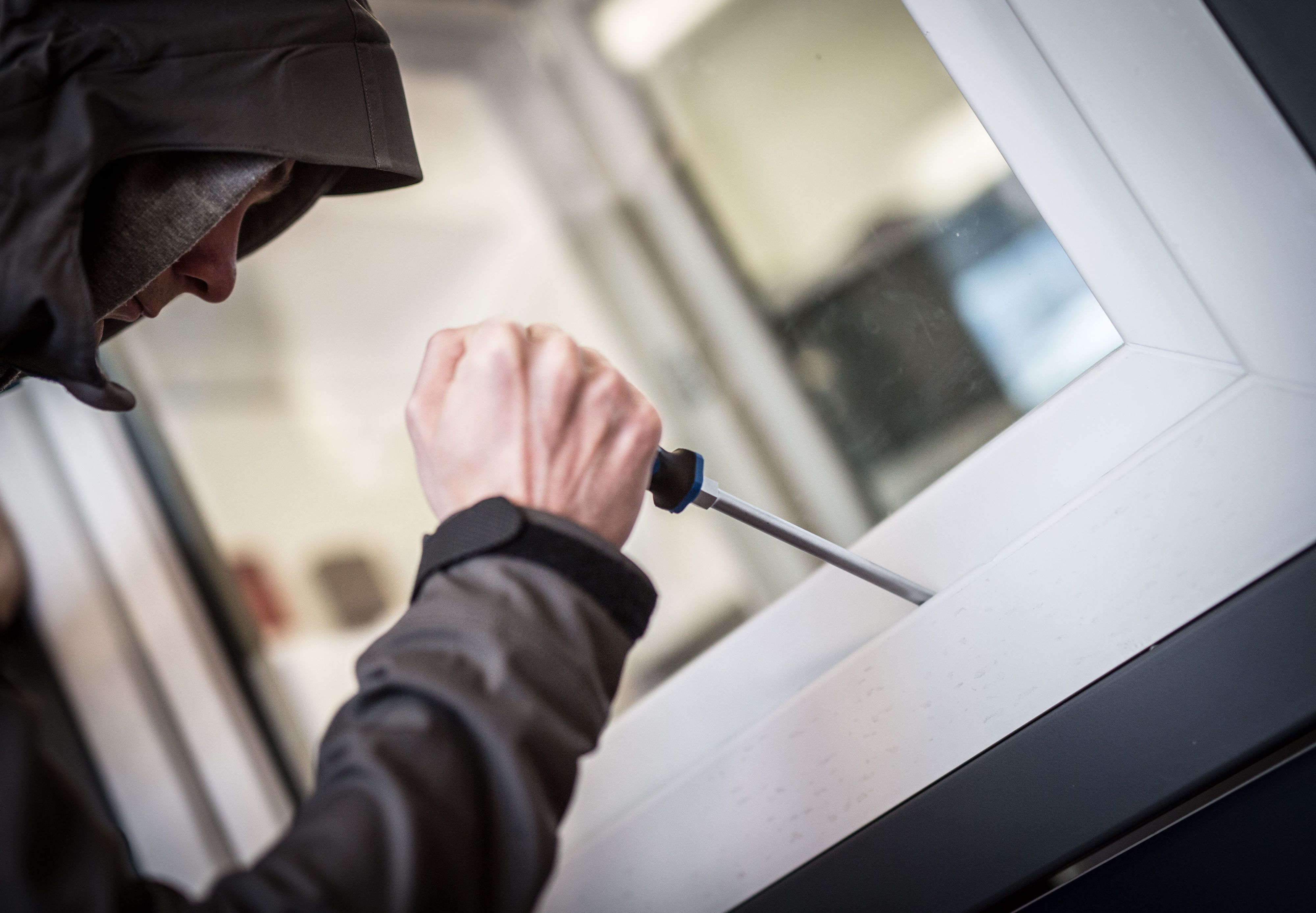 Ein Mann hebelt ein Fenster mit einem Schraubendreher auf (Illustration)