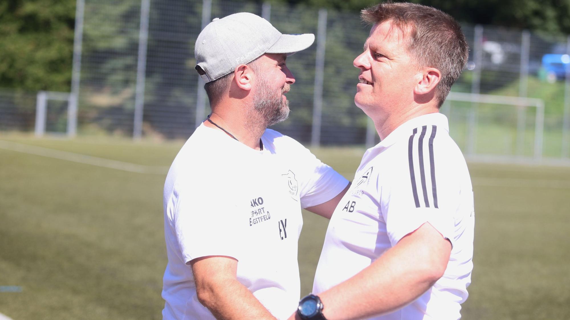 Zu sehen sind zwei Fußballtrainer, die einander die Hände geben.