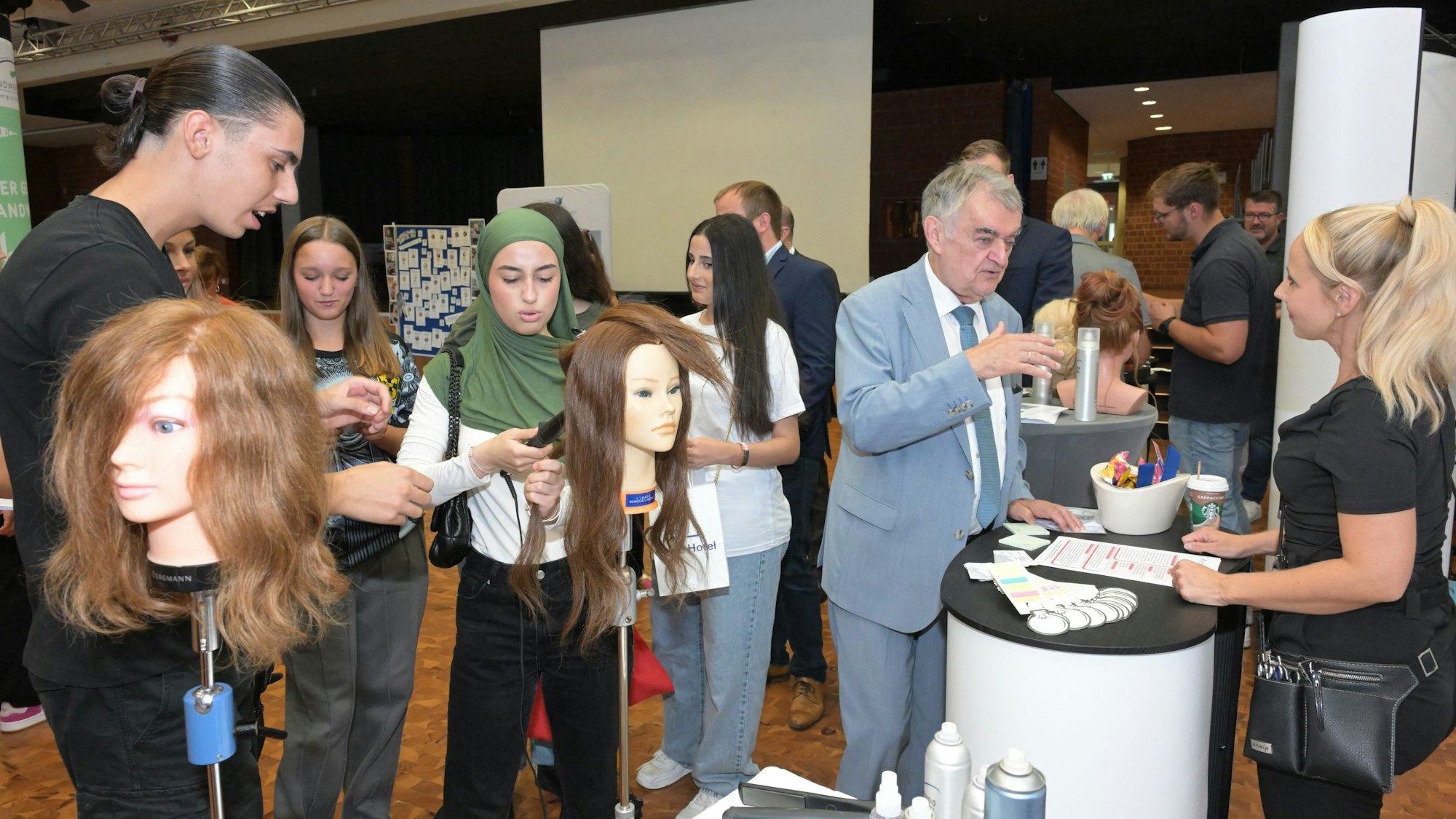 NRW-Innenminister Herbert Reul besucht die Ausbildungsmesse in Overath. Jugendliche schauen sich Perückenköpfe an.