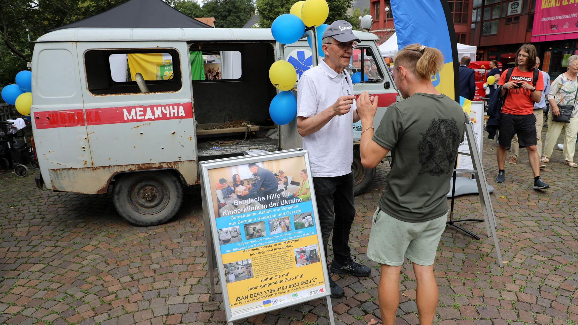 Zwei Menschen stehen vor einem zerschossenen ukrainischen Krankenwagen auf dem Stadtfest in Bergisch Gladbach.